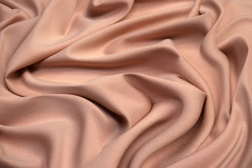 Smooth peach-colored synthetic fabric draped in folds, highlighting man-made textile properties.