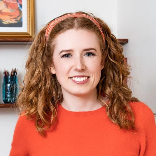 Alison Hoenes, a smiling female fashion designer with curly reddish-blonde hair and an orange sweater, looking friendly and approachable for a professional profile or author photo.