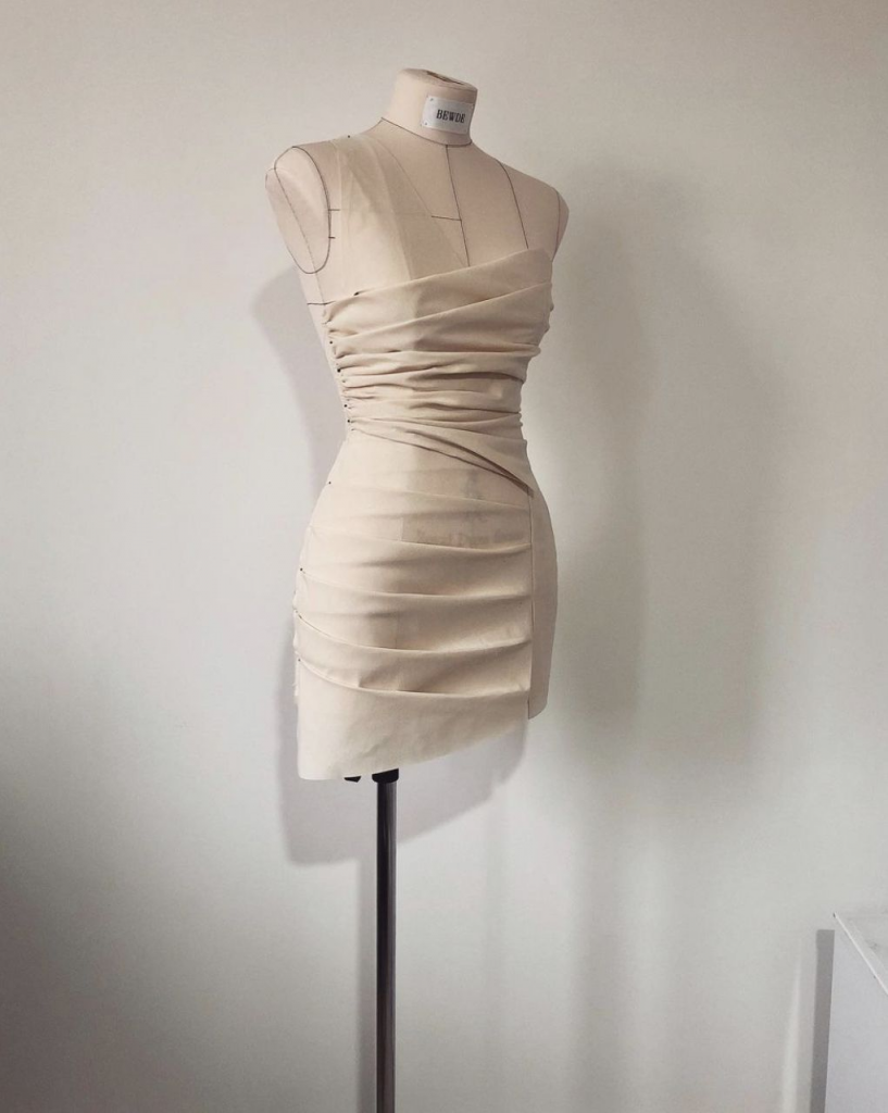 Pattern making and draping class example: A beige cocktail dress being draped and pinned directly onto a dress form, a core skill taught in fashion courses in India.