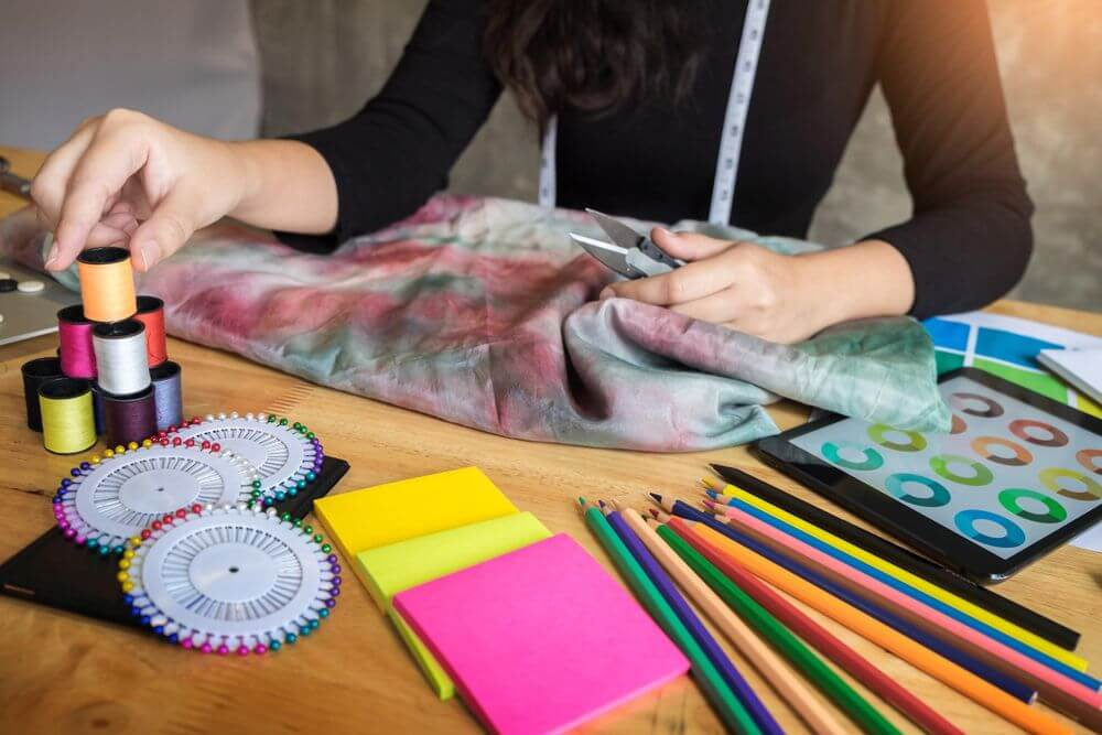 Close-up of a designer working on tie-dye or patterned fabric with spools of thread and drawing tools, ideal illustration for a practical textile design course in India for housewives and working professionals.