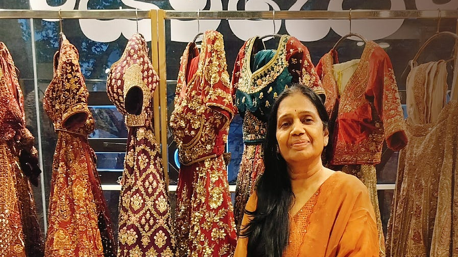 Successful boutique owner Kusum Agarwal standing in front of high-end embroidered Indian bridal lehengas and ethnic wear.