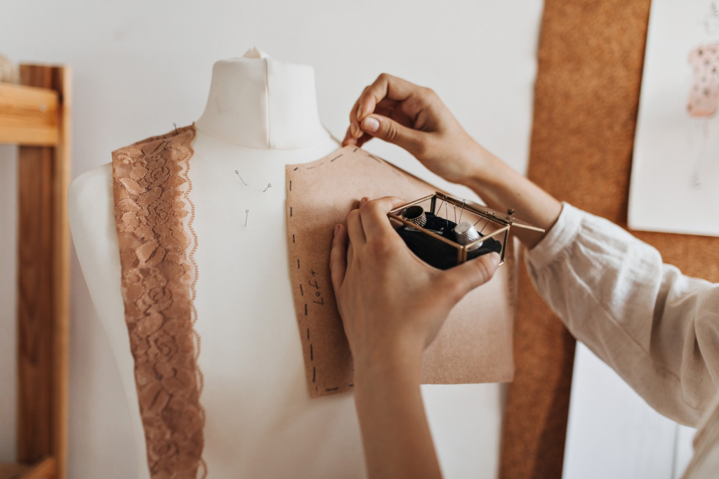A fashion designer pinning a brown paper pattern to a white dress form mannequin for garment construction.