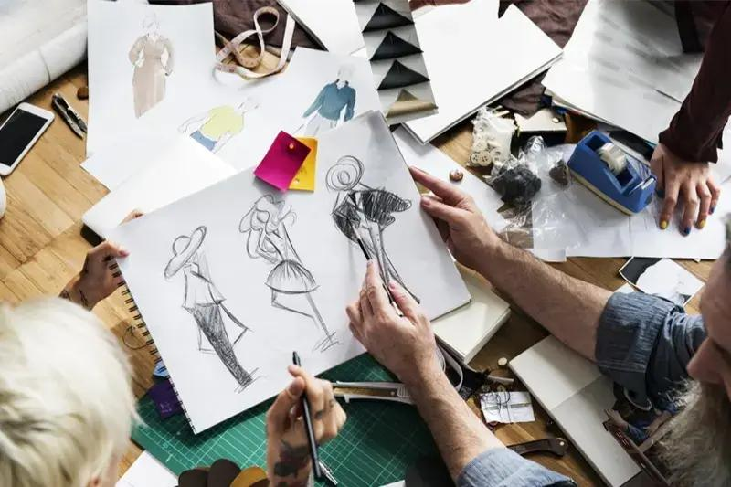 Fashion designing students sketching clothing concepts and creating garment designs on paper in a studio workspace