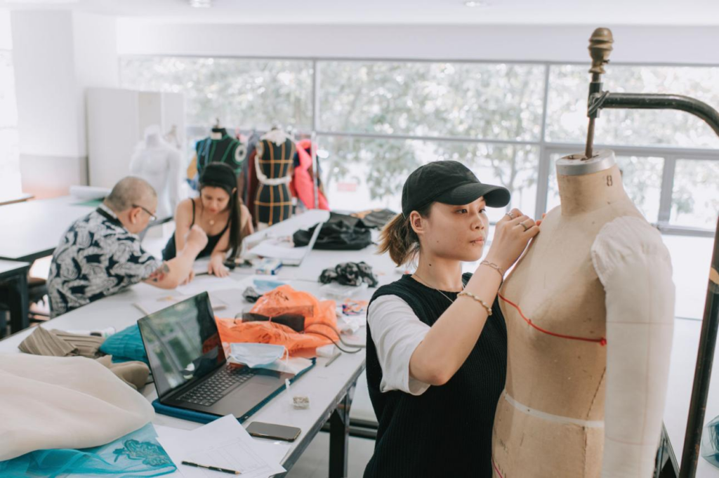 Fashion design student working on garment fitting using a dress form in a professional fashion design classroom
