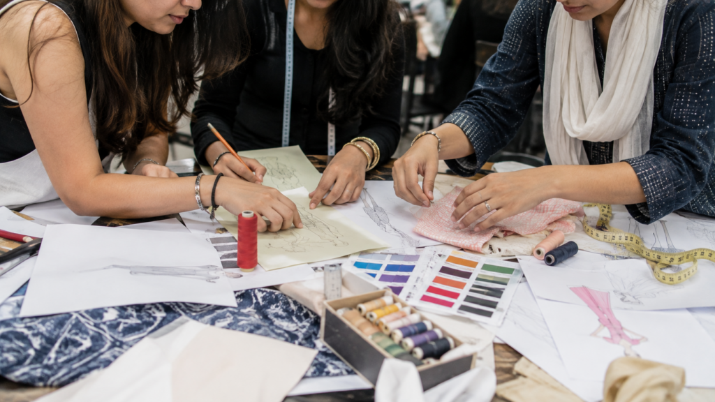 Fashion design students collaborating on garment sketches, fabric selection, color palettes, and pattern planning during a hands-on design workshop.